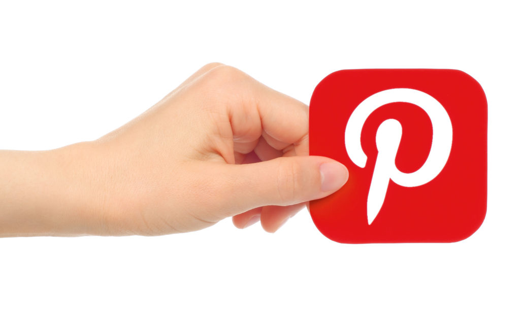 Person's hand holding icon for Pinterest, red with white P.