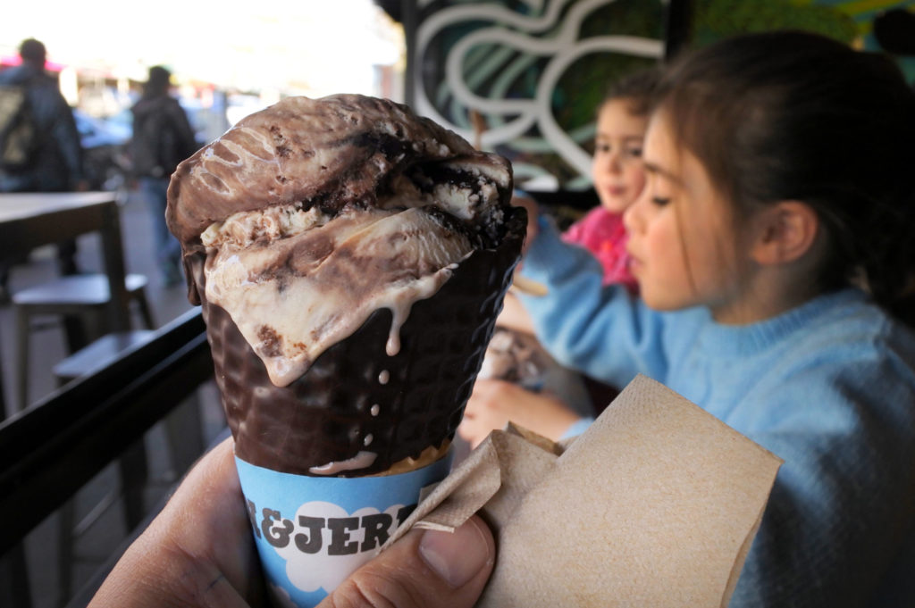A hand holds up a Ben & Jerry's ice cream cone in front of two girls also eating ice cream as a social media post for content development